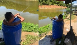 Người đàn ông ngồi hẳn trong thùng phuy vừa ngâm mình tránh nóng 40 độ, vừa thư giãn câu cá