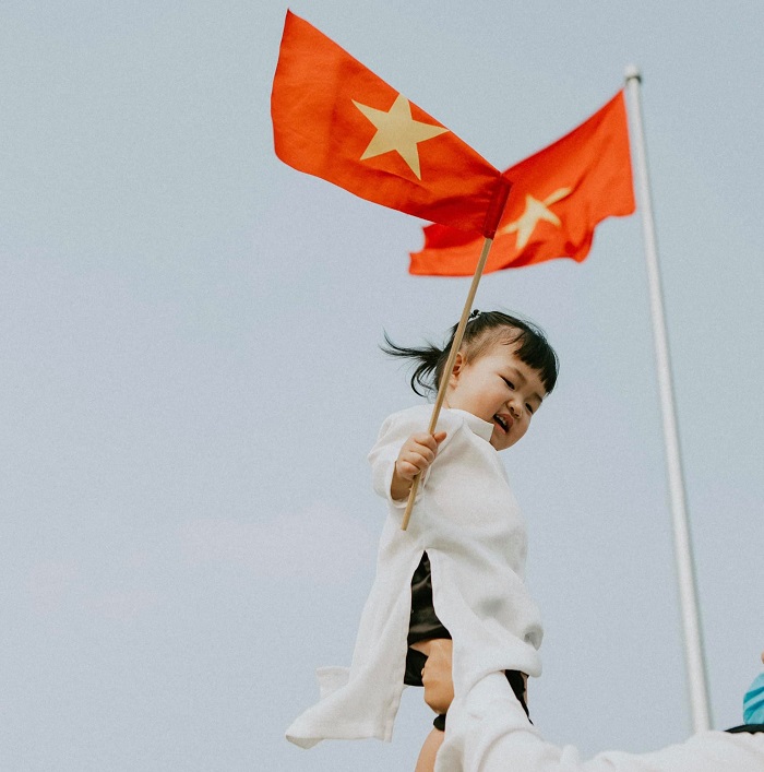 Em bé Việt Nam mặc áo dài trắng, cầm cờ đỏ sao vàng giữa tâm dịch: Cố lên Việt Nam ơi! - Ảnh 1 Em bé Việt Nam mặc áo dài trắng, cầm cờ đỏ sao vàng giữa tâm dịch: Cố lên Việt Nam ơi! - Ảnh 1
