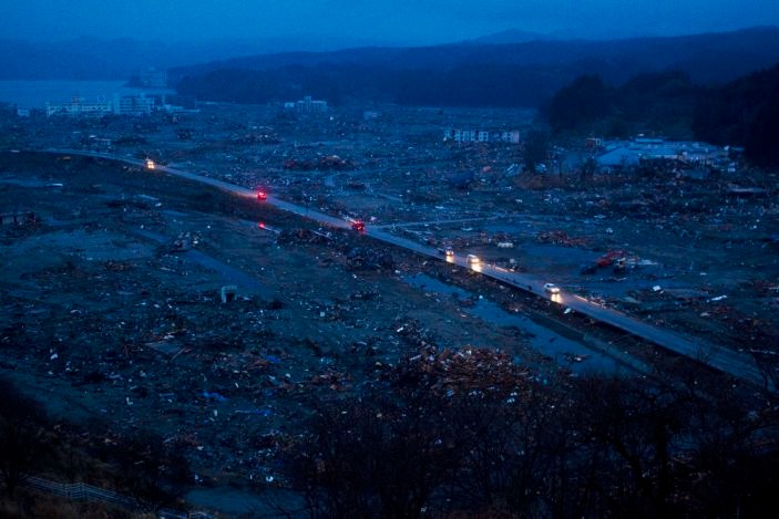 Vào ngày 15/3/2011, các phương tiện giao thông đi qua đống đổ nát bị san bằng sau trận động đất, sóng thần tại Minamisanriku, tỉnh Miyagi. Ảnh: AP