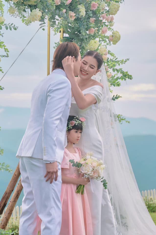 Không gian ngoài trời với rực rỡ sắc hoa khiến nhiều người liên tưởng đến câu chuyện cổ tích. Cô dâu diện thiết kế váy cúp ngực, ôm sát hình thể. Cựu người mẫu lựa chọn lúp đội đầu dài quết đất. 